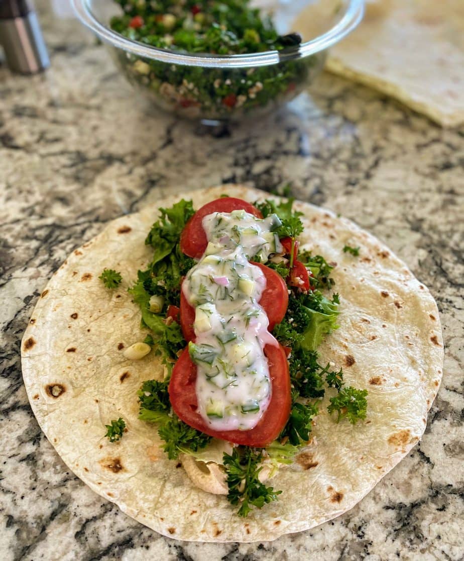 Sliced tomatoes and vegan tzatziki added to the hummus and Tabbouleh  wrap on the counter