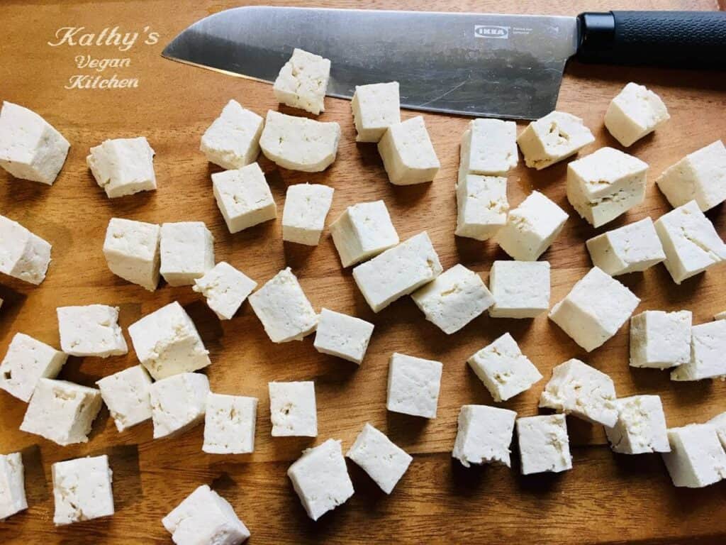 Tofu is cut into cubes on the acuttingboard with a knife.