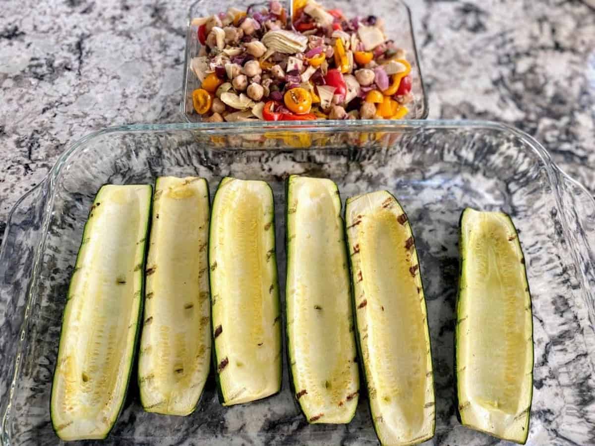Grilled zucchini boats in a pan with the filling in a separate bowl behind it on the counter