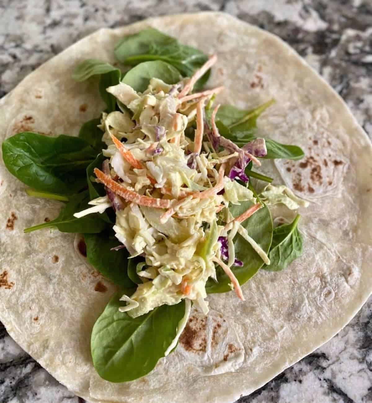 tortilla on a counter with spinach and coleslaw