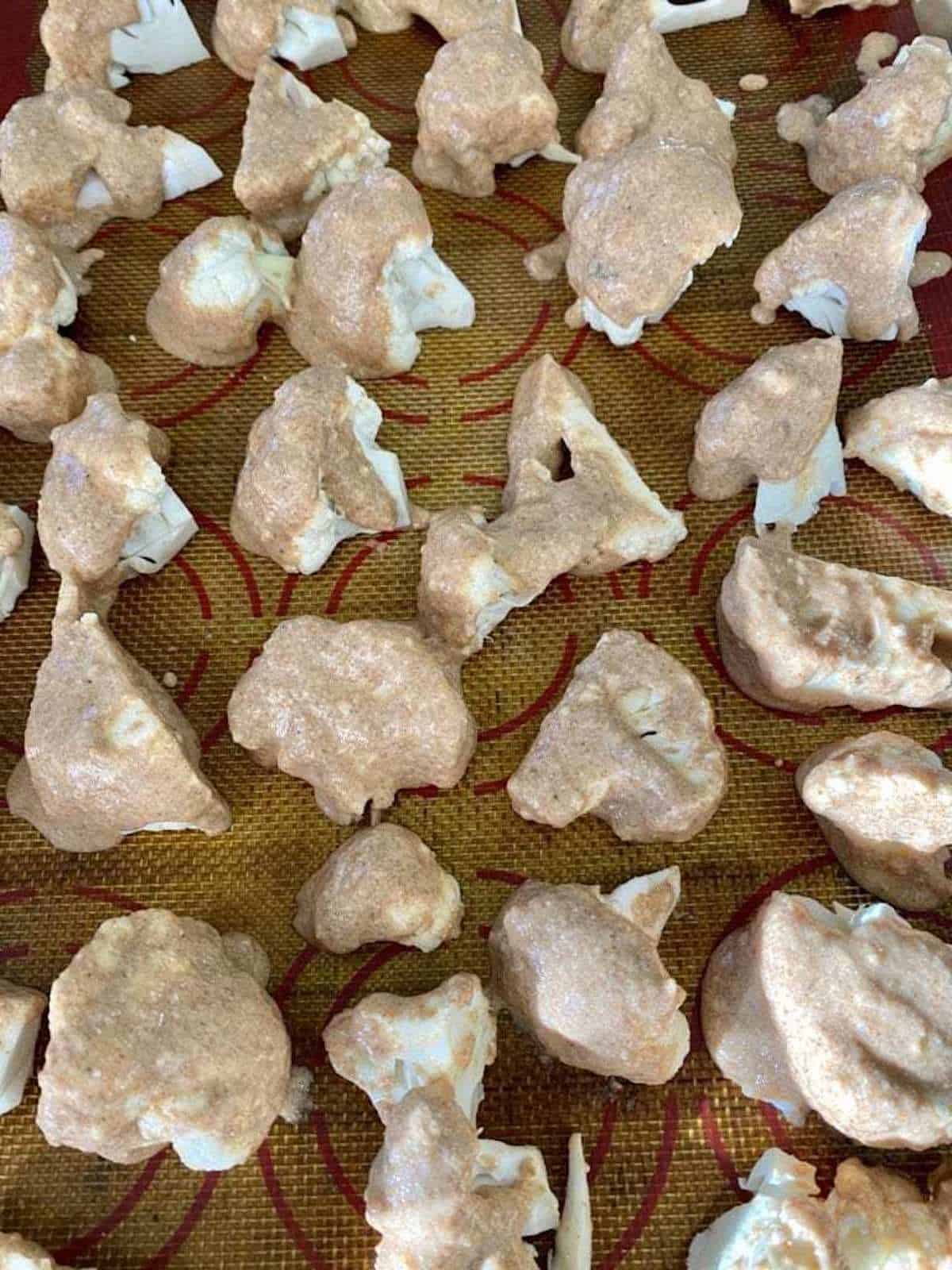 Cauliflower florets are dipped in flour on a baking sheet