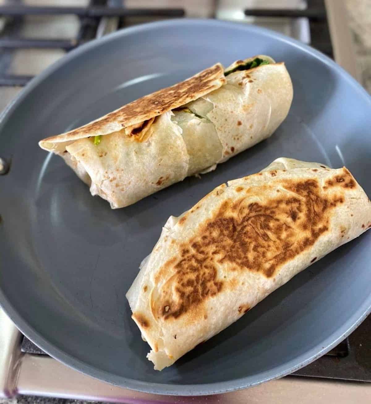 Two wrap sandwiches in a skillet grilling on the stove
