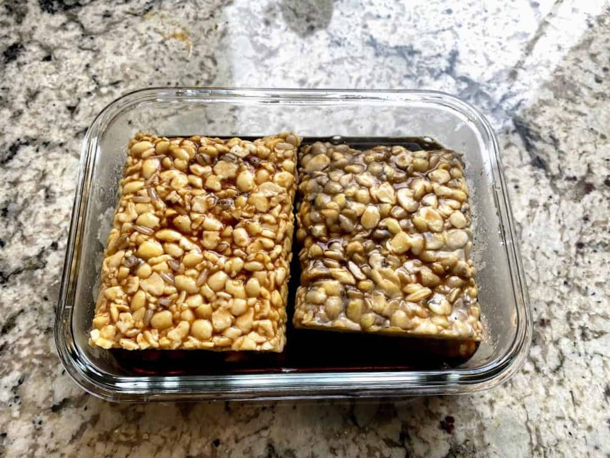 Boiled tempeh in a a container with marinade on the counter