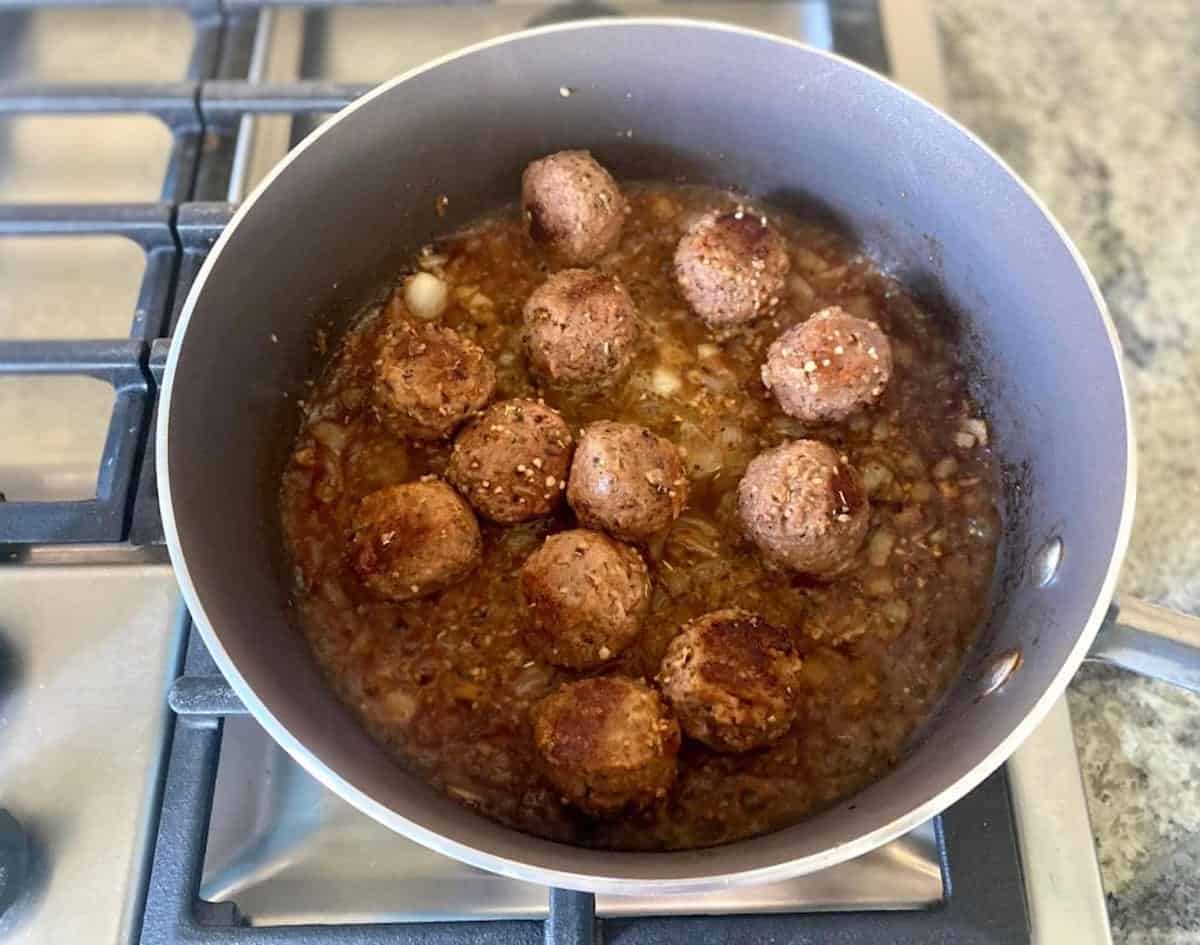 Frozen meatballs added to the sautéed onions in a skillet on the stove