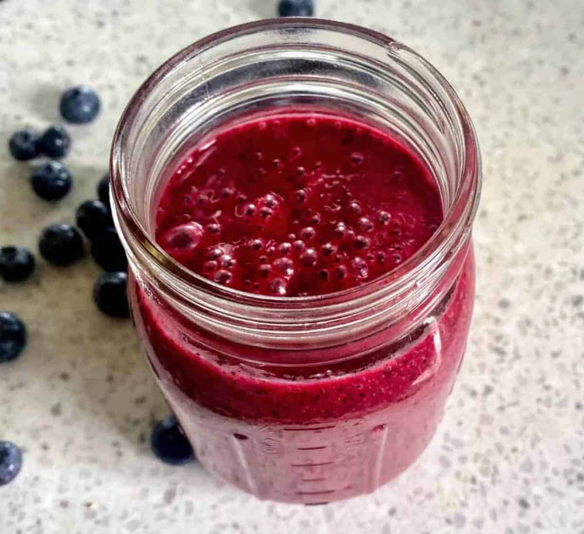 Blueberry dressing in a mason jar on the counter with blueberries surrounding the jar
