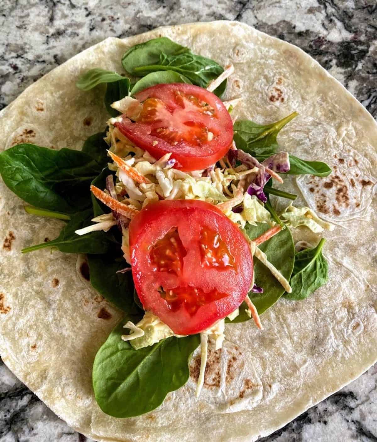Slices of tomato added to the tortilla with spinach and coleslaw on the counter