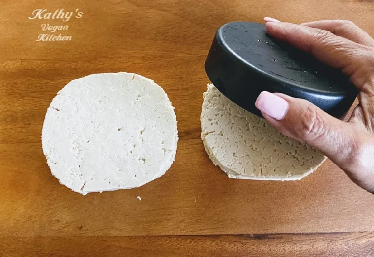 Two circular pieces of tofu cut using a burger press on a cutting board
