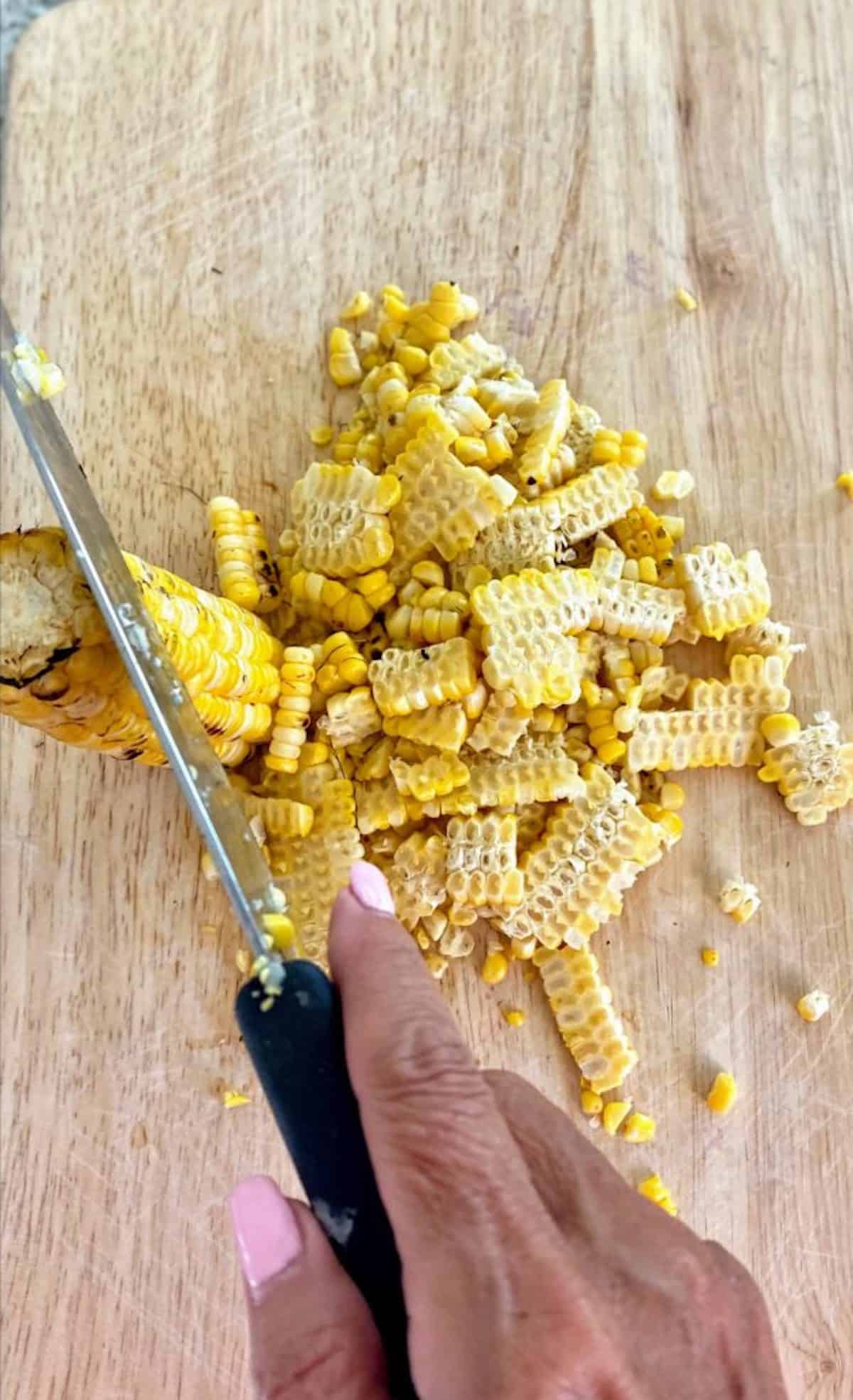 Cutting corn off the cobs on a cutting board on the counter