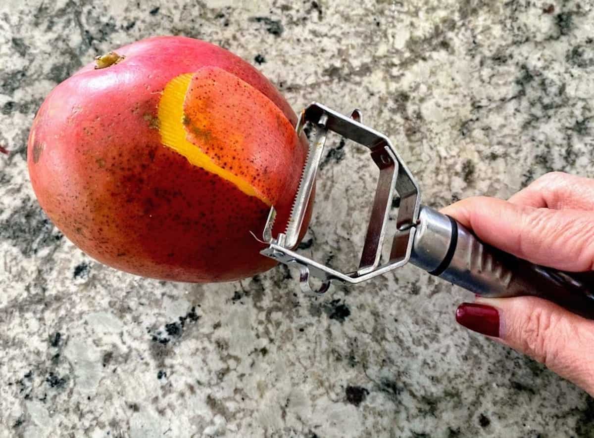 Peeling mangoes with a vegetable peeler on the counter