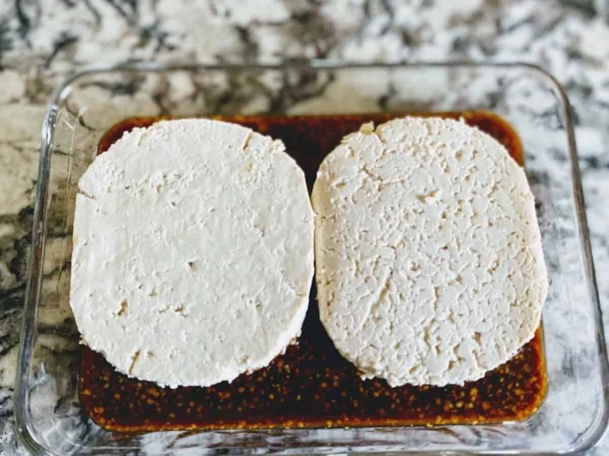 tofu burgers marinating in a refrigerator safe dish before refrigerating
