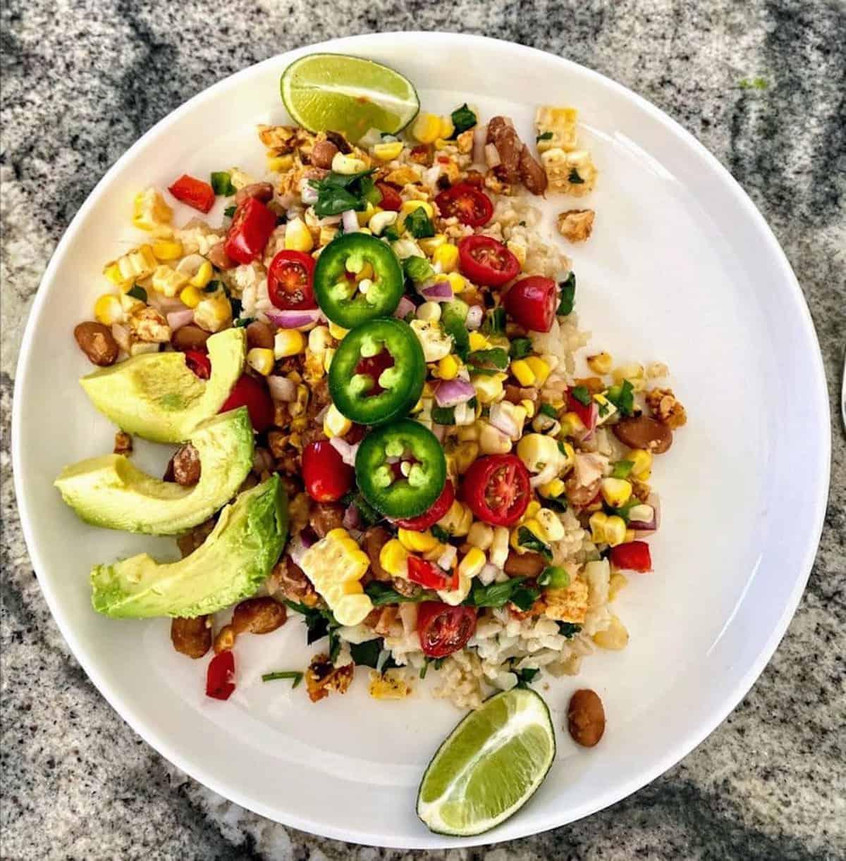 Vegan Chipotle Bowl in a bowl garnished with avocado, limes, tomatoes and jalapeños. 