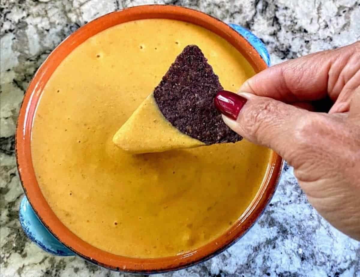 Skinny nacho cheese sauce in a bowl with a blue tortilla chip dipped in the center.