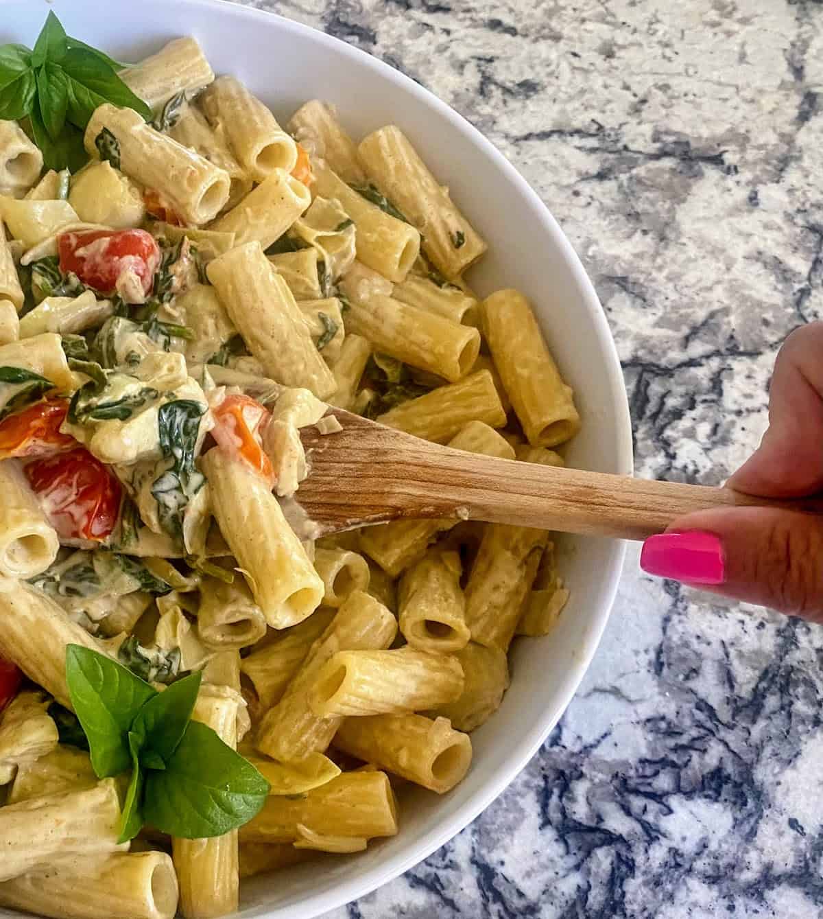 Spinach artichoke pasta in a bowl stirring with a wooden spoon.