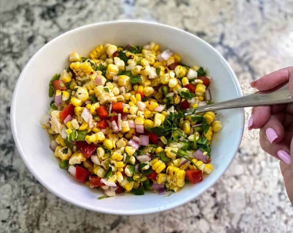 Corn salsa in a bowl on the counter with a spoon in it. 