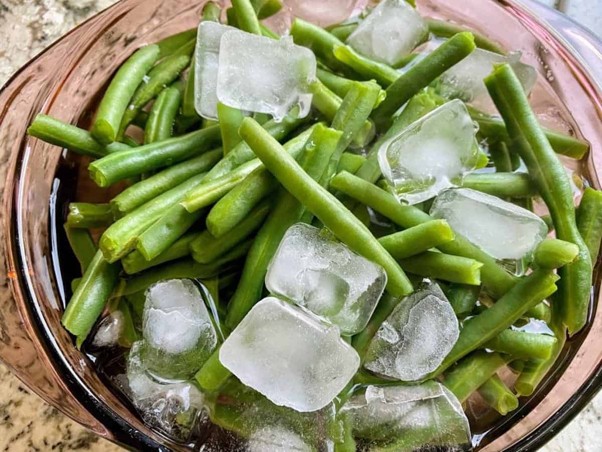 Green beans in a bowl with ice cubes and water on the table.