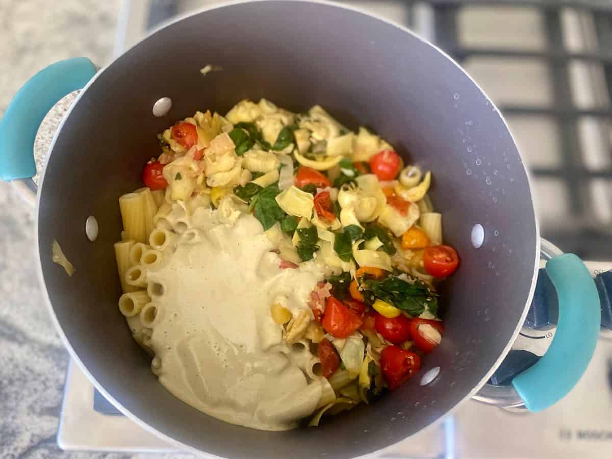 I am adding cashew cream, tomatoes, spinach, and lemon juice into a pot on the stove.