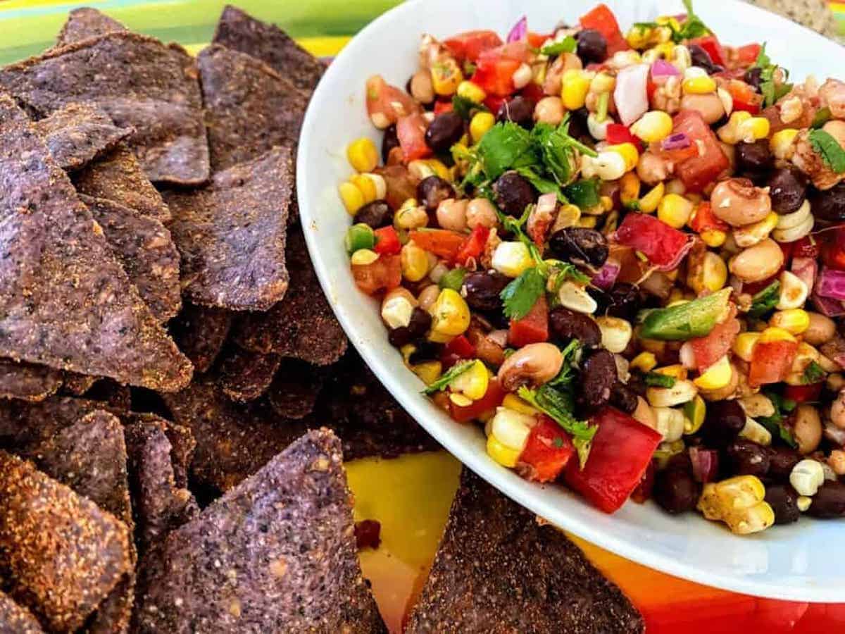 Bean salsa in a bowl with blue corn chips on a plate