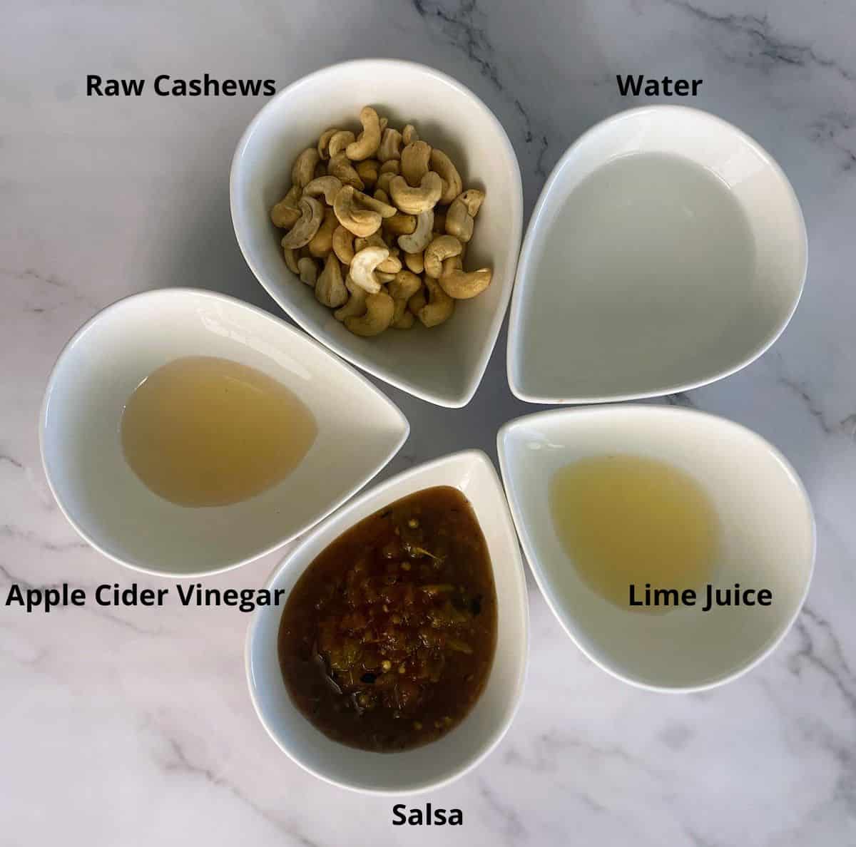 Vegan Southwest Dressing Ingredients in bowls: Raw cashews, water, lime juice, salsa, apple cider vinegar on the table
