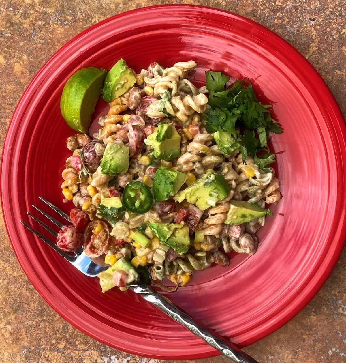 Taco pasta salad served on a red plate with a lime wedge, avocado and cilantro as a garnish