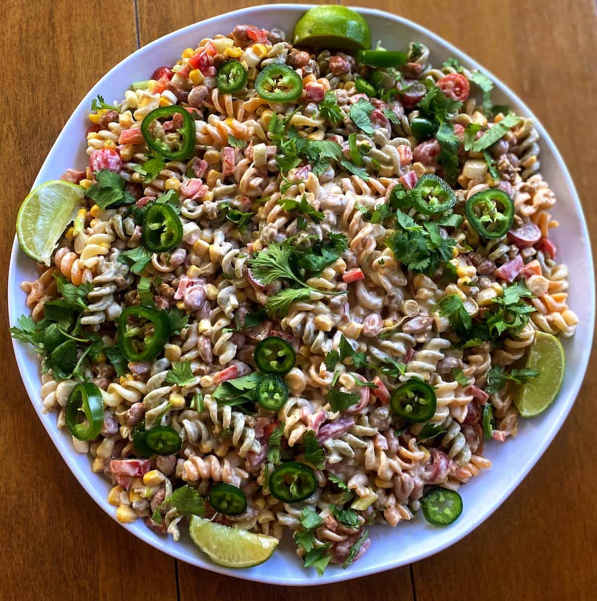 taco pasta salad on a tray garnished with limes, cilantro and jalapeno slices on the table.