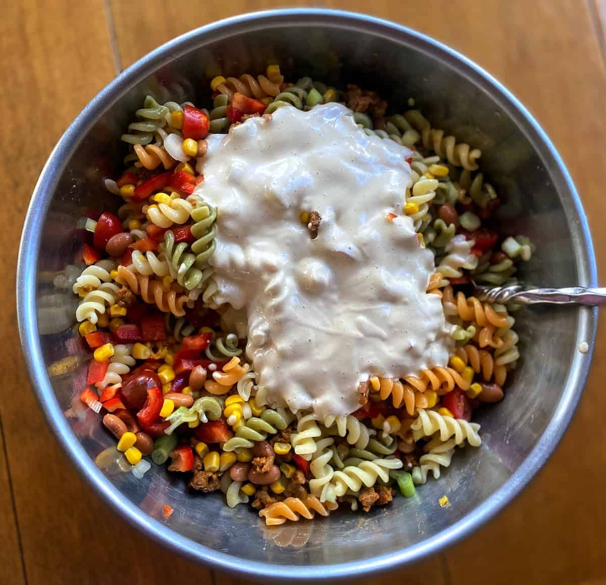 Vegan southwest dressing poured into the bowl of stirred ingredients on the table.
