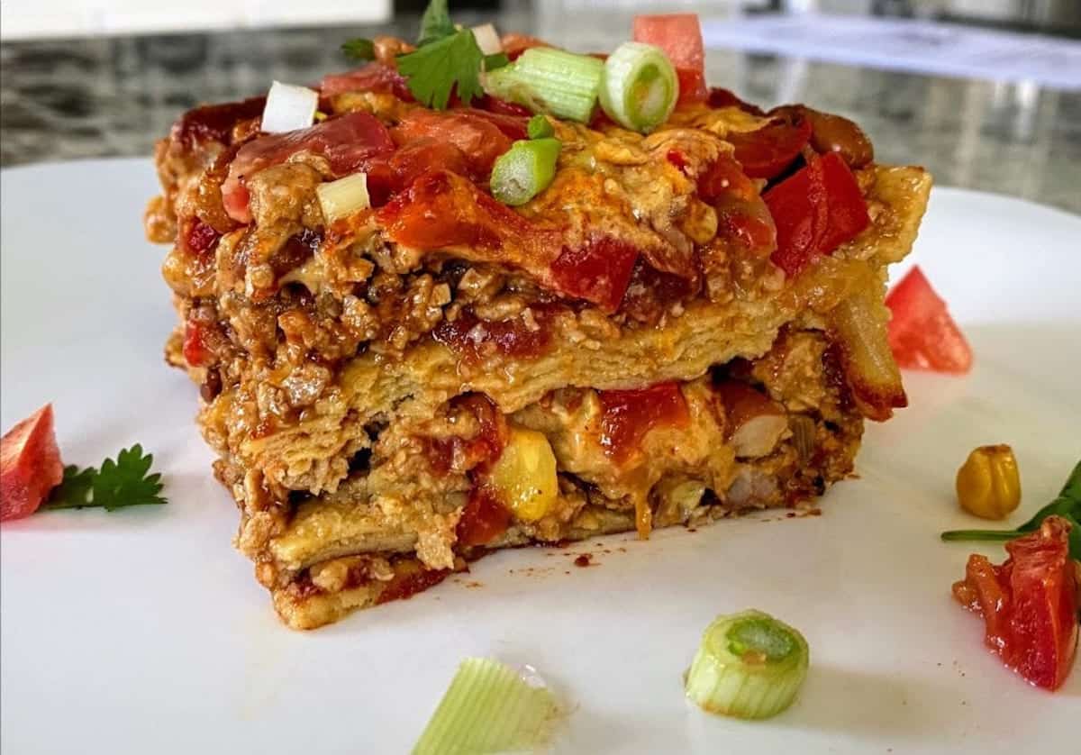 Slices of enchilada casserole on a plate garnished with green onions, cilantro and Roma tomatoes.