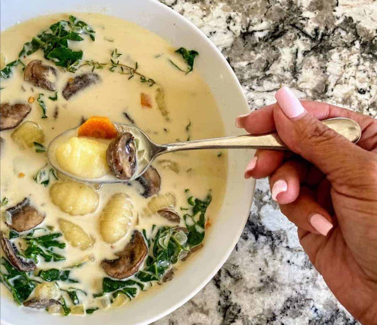 Vegan gnocchi soup recipe served in a bowl with a spoon on the table.