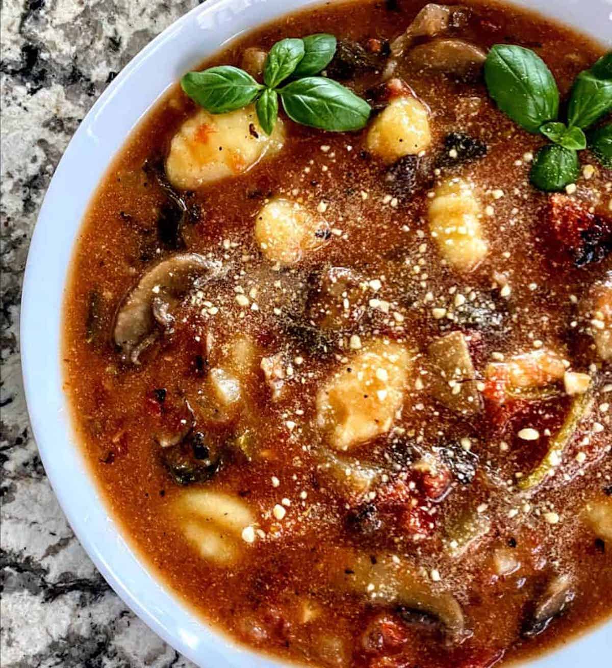 Tomato gnocchi soup in a bowl garnished with vegan parmesan cheese and basil 