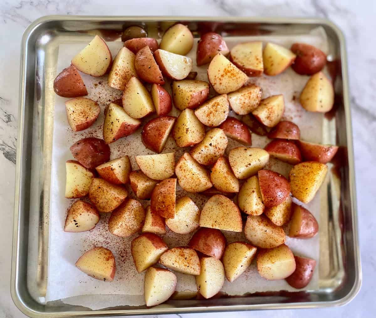 Parboiled potatoes on a baking sheet with parchment paper sprinkled with paprika. 