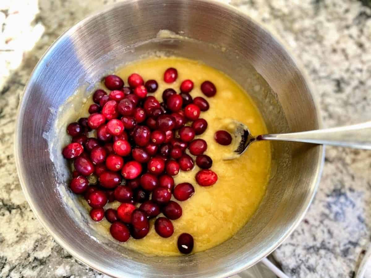 I am folding cranberries into the batter in a bowl.
