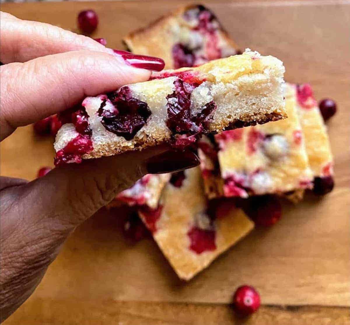 Holding a vegan cranberry bar. Other cranberry bars on the cutting board.
