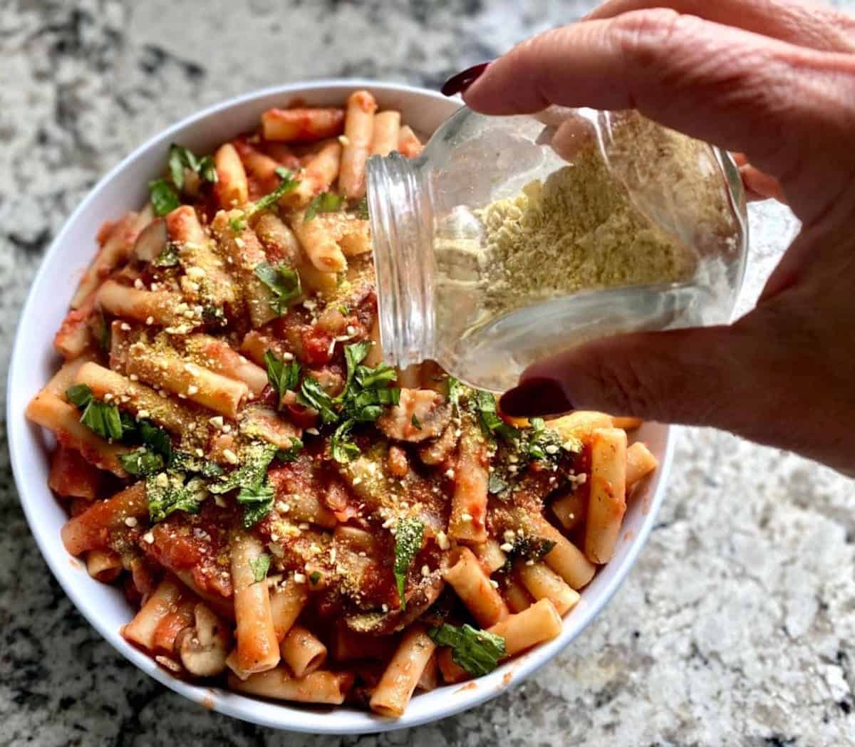 Sprinkling the creamy tomato pasta recipe with vegan parmesan cheese. 