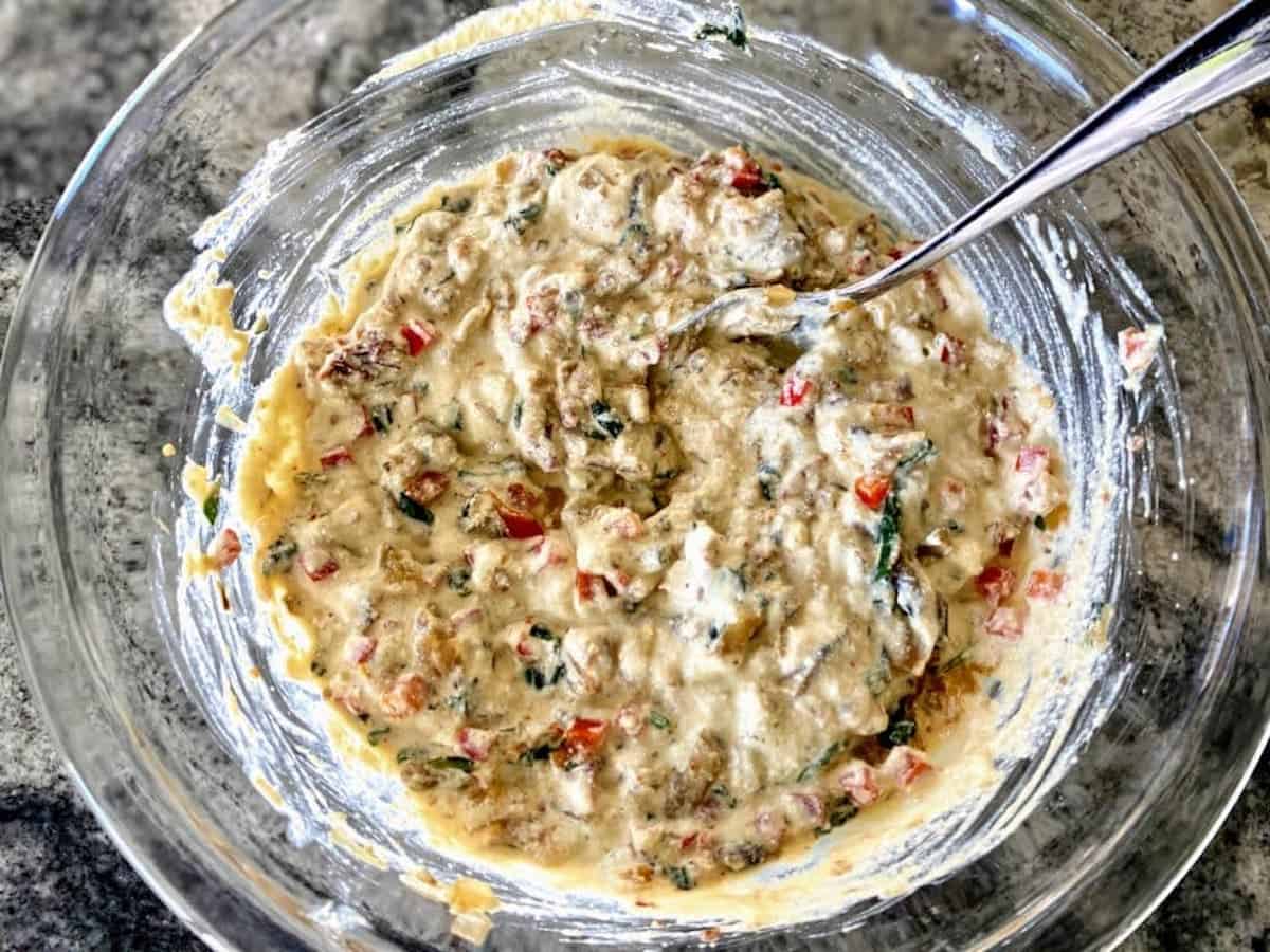 Mixed vegan quiche batter on the table with a spoon in the bowl for the vegan quiche recipe.  