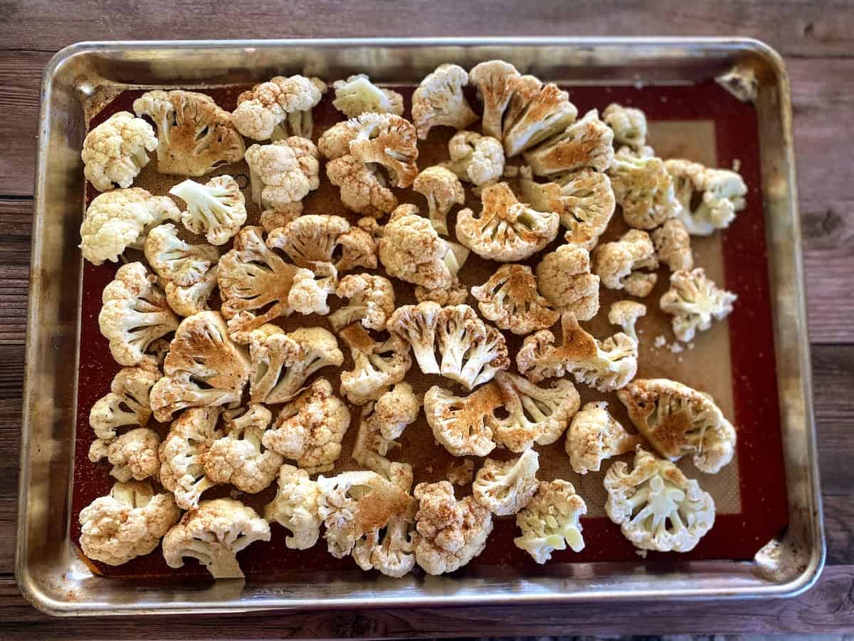 Cauliflower florets on a baking sheet with taco seasoning sprinkled on the florets.