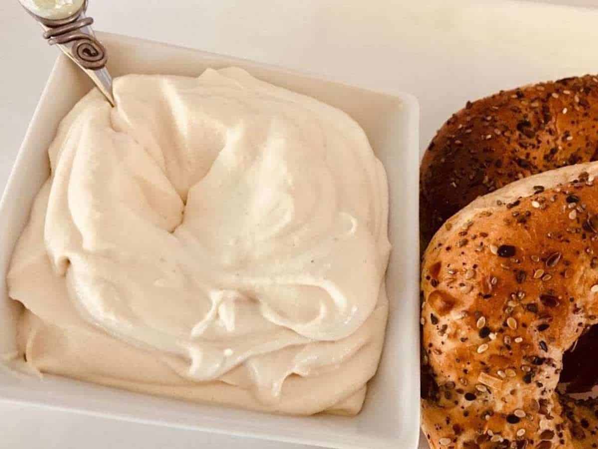 Vegan cream cheese recipe in a bowl with a spoon and bagels on the plate.