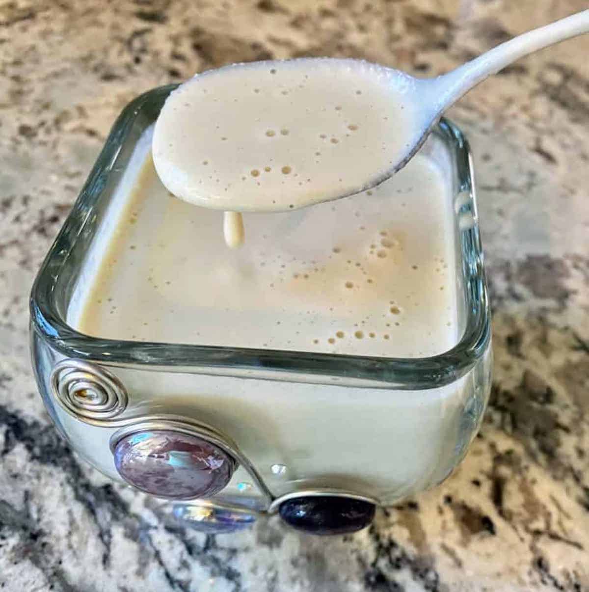 I am putting a spoon into a glass dish with vegan dressing. 