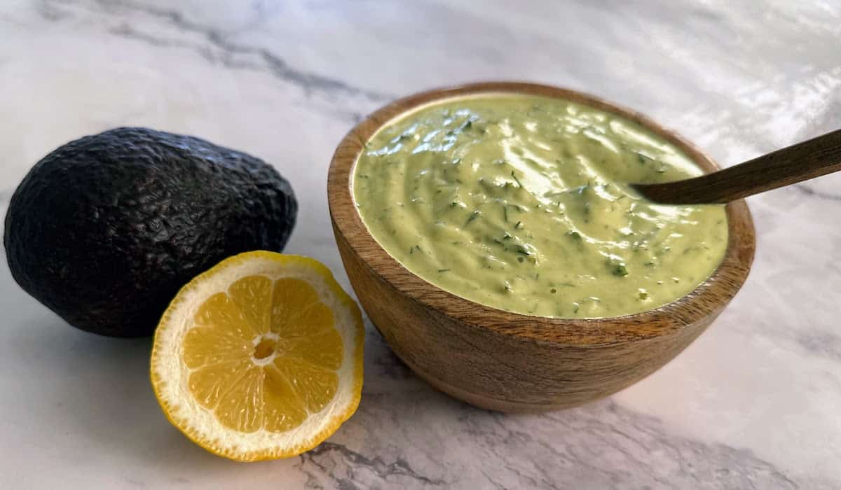 Avocado ranch dressing in a bow with a lemon and an avocado on the table.