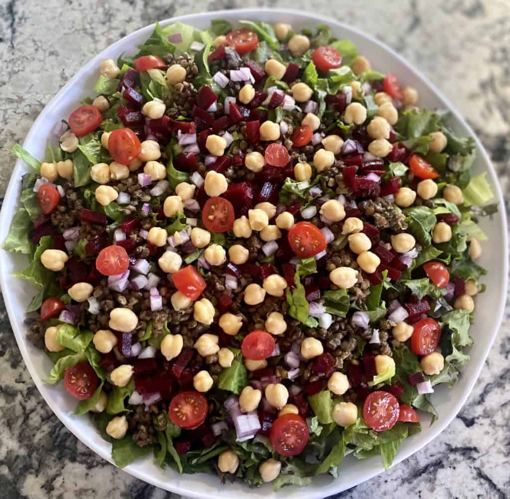 Chopped vegan Greek salad ingredients layered on top of green and lentils. 