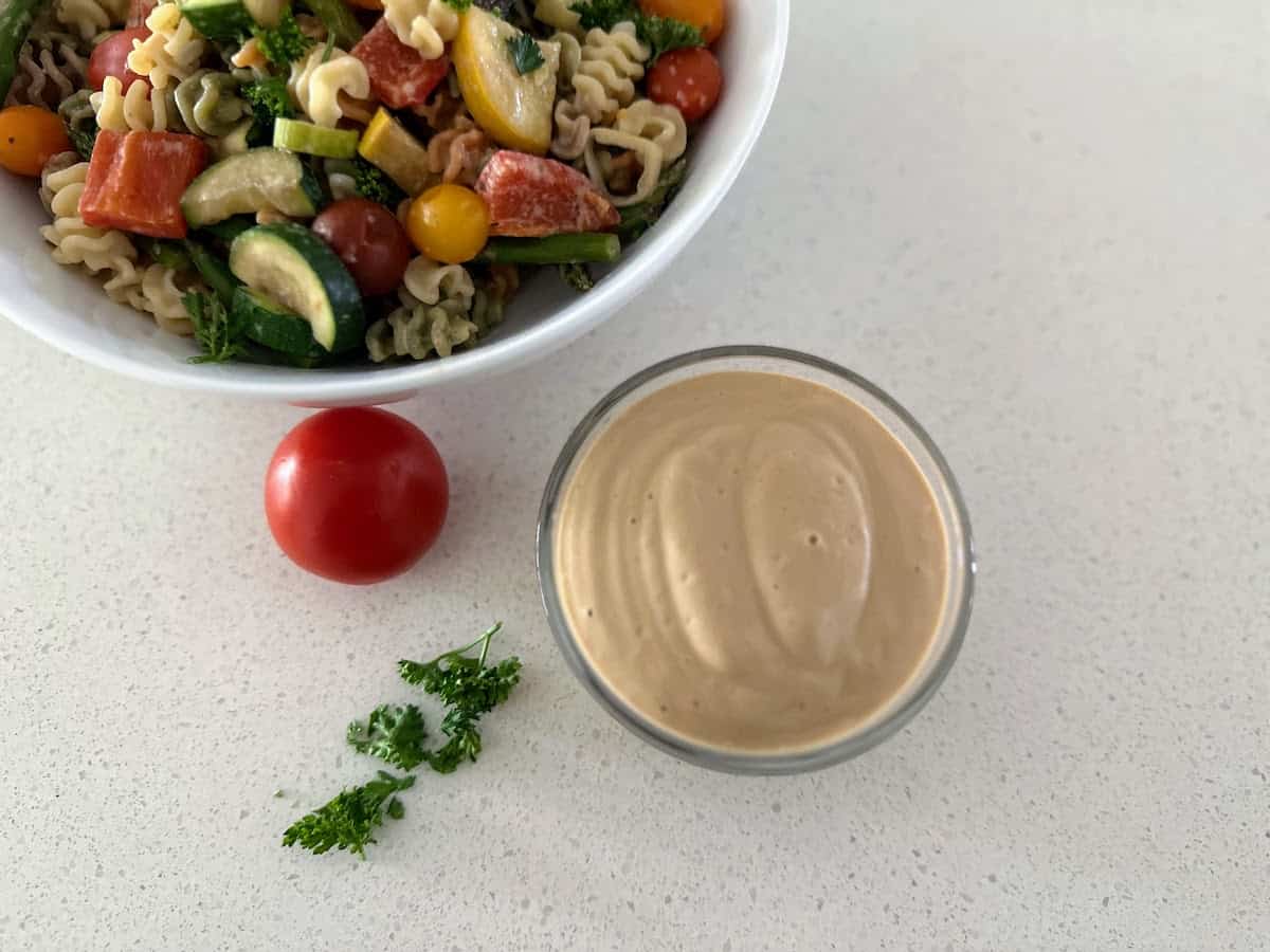 Creamy balsamic vinegar dressing ina bowl next to a salad on the counter. 