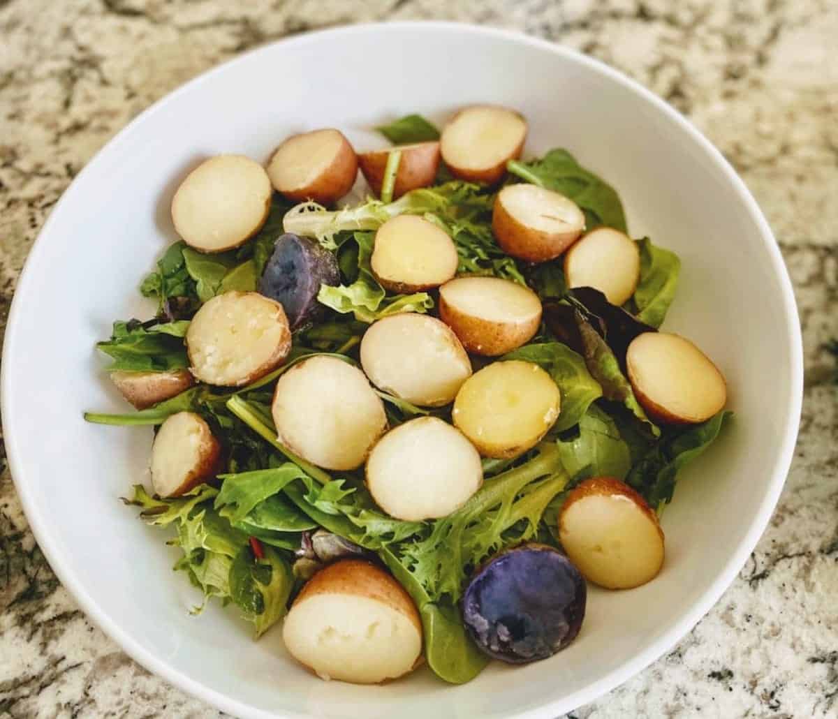 Cooked new potatoes in a bowl with salad greens for the Tuscan chopped salad recipe.