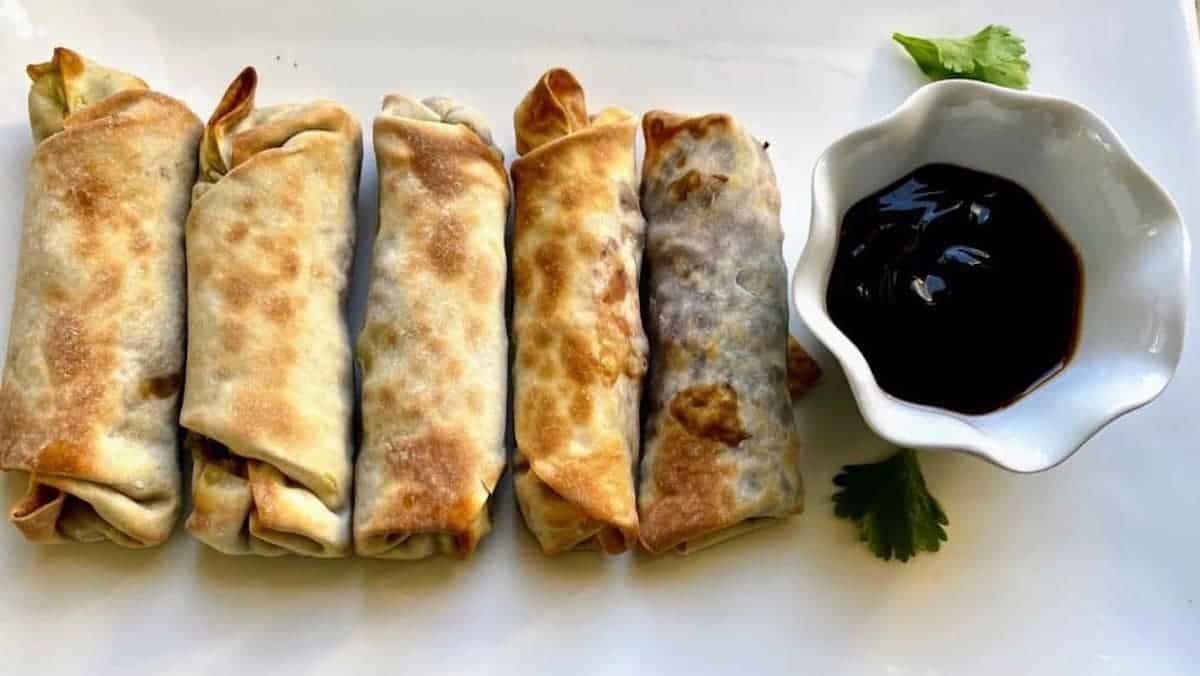 Vegan avocado egg rolls on a plate with dipping sauce.