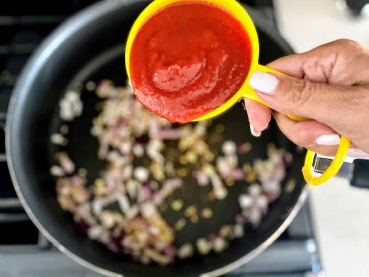 I am adding tomato passata to the pan of garlic and onions.