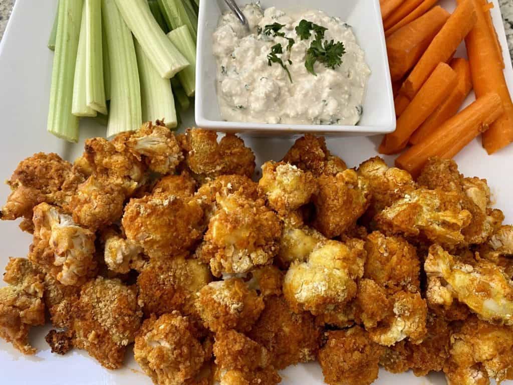 Vegan buffalo cauliflower bites recipe on a platter with celery, carrots and blue cheese dressing.