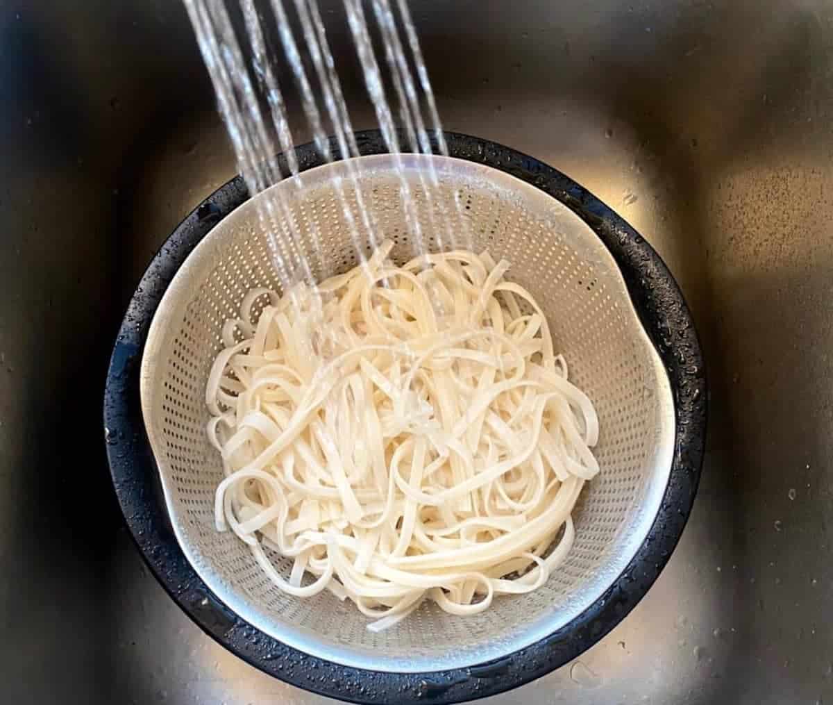 I am rinsing the rice noodles in a colander in the sink. 