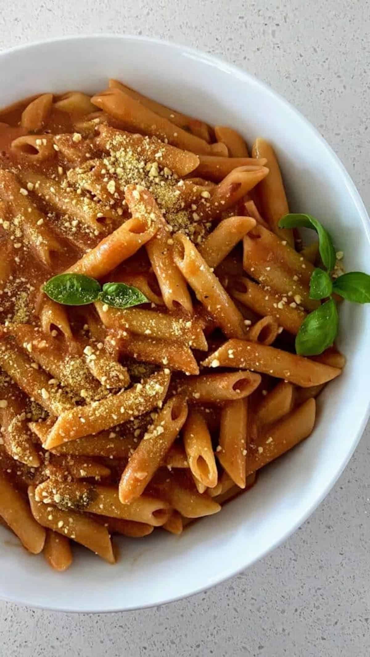 Rose Penne in a bowl with fresh basil and vegan parmesan cheese.
