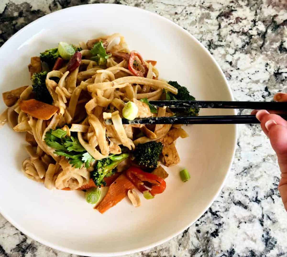 Vegan Pad Thai recipe on a plate. I am eating it with chop sticks. 