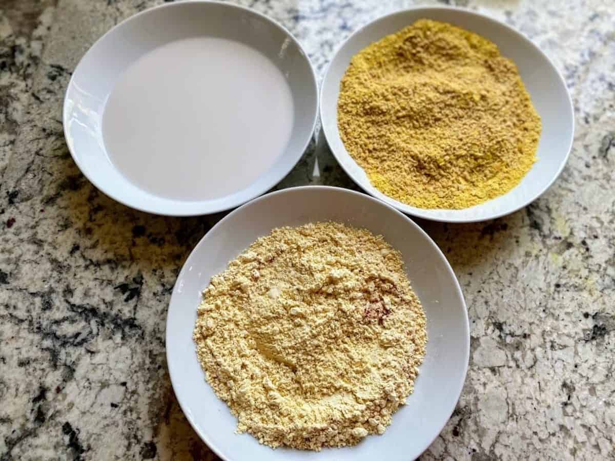 Three dredging bowls: plant milk, nutritional yeast and breadcrumbs, and paprika and chickpea flour.