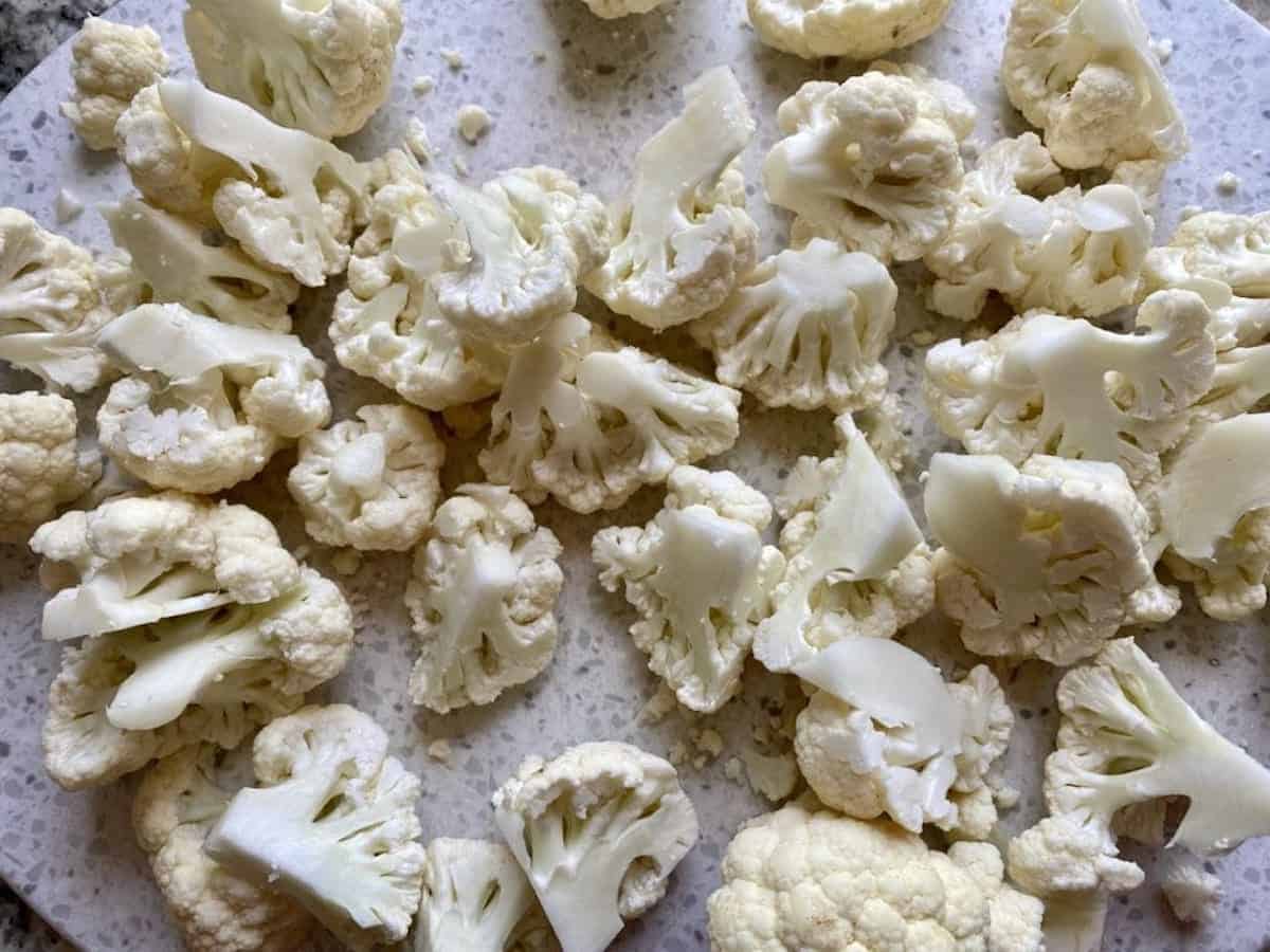 Cut cauliflower florets on a cutting board.