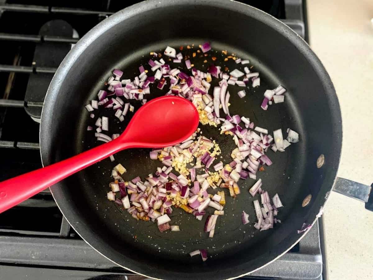 Red onion and garlic are cooked in a skillet on the stove.