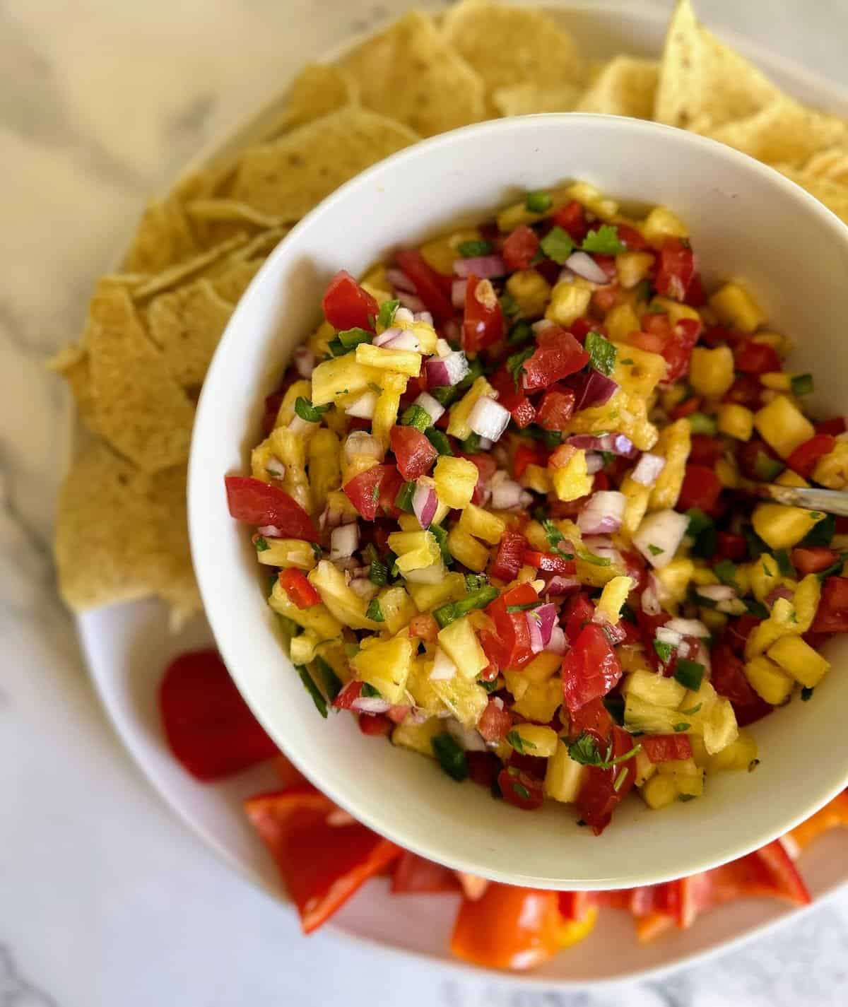 Easy pineapple salsa ina bowl served with tortilla chips and baby bell peppers. 